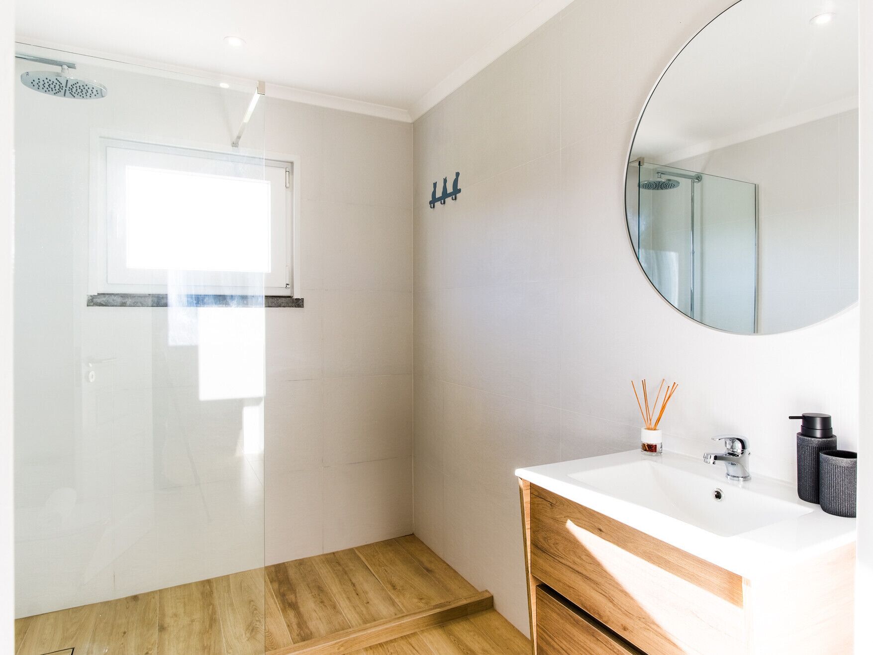 Un bany modern amb dutxa, un lavabo amb mirall i un terra de fusta.