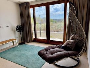A room with a large sliding glass door, a hanging chair, a standing fan, and a small bench.