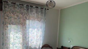 Une chambre à coucher avec un lit en bois, un mur vert et une fenêtre ornée de rideaux à motifs de bambou.