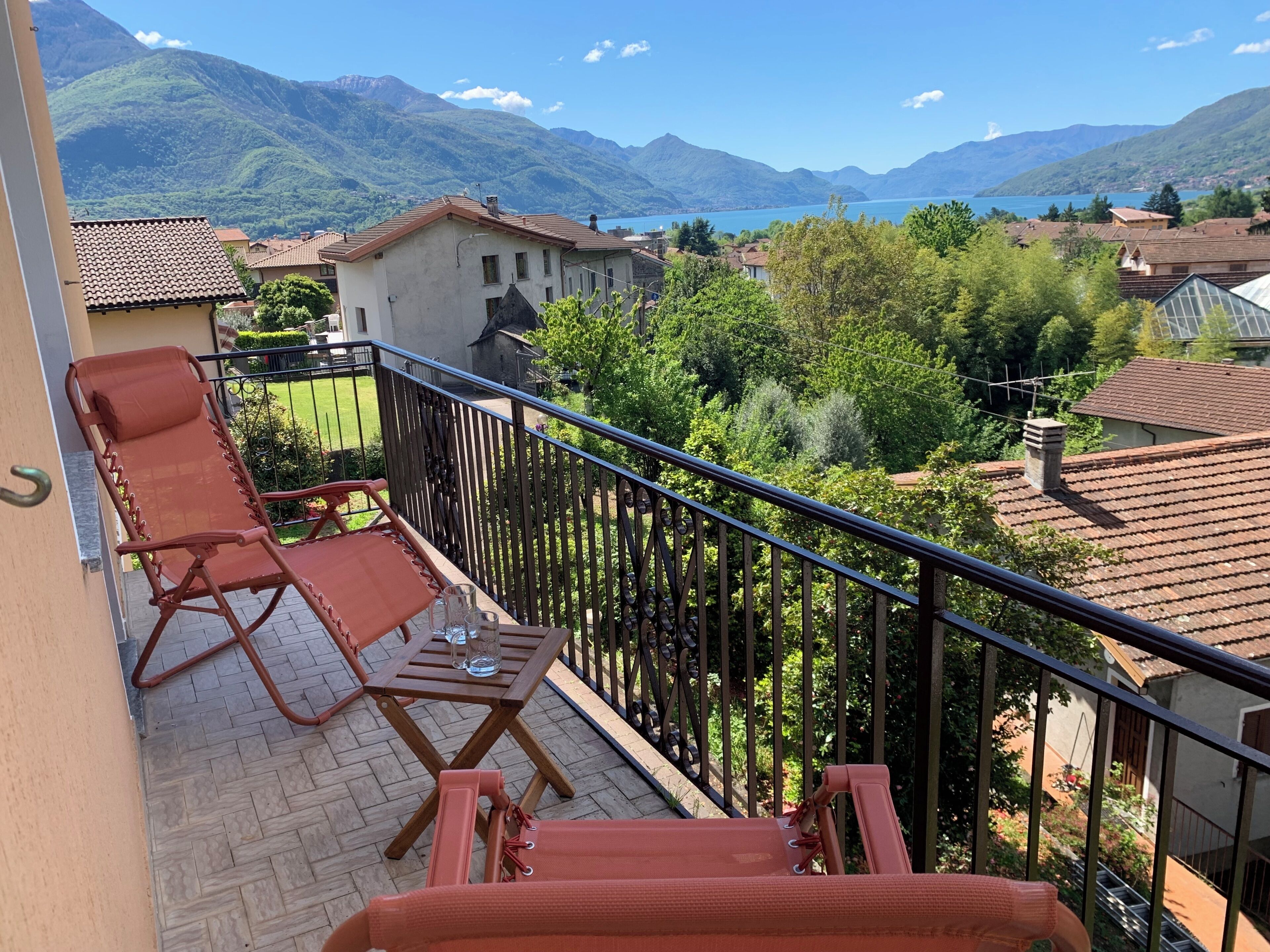 Ein Balkon mit zwei Liegestühlen und einem Tisch, mit Blick auf eine Berglandschaft und einen See.