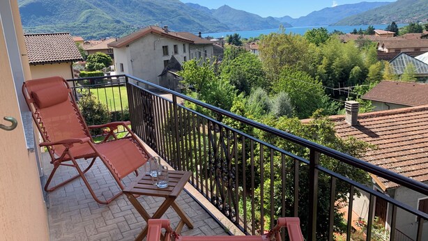 Un balcon avec deux fauteuils et une table, offrant une vue sur un paysage montagneux et un lac.