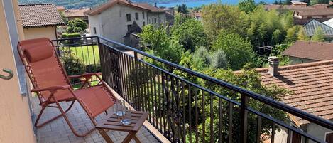 En balkon med to liggestole og et bord, med udsigt over et bjerrelandskab og en sø.