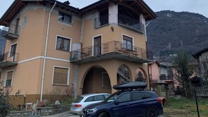 Un immeuble résidentiel à plusieurs étages, doté de balcons, d’une allée pavée et surplombant un paysage montagneux.