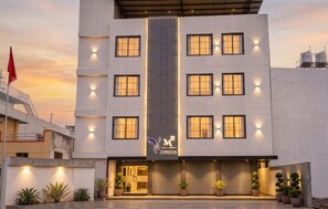 A modern hotel with a central vertical light strip, multiple windows, and a closed garage door. - M Square Express (Jabalpur)