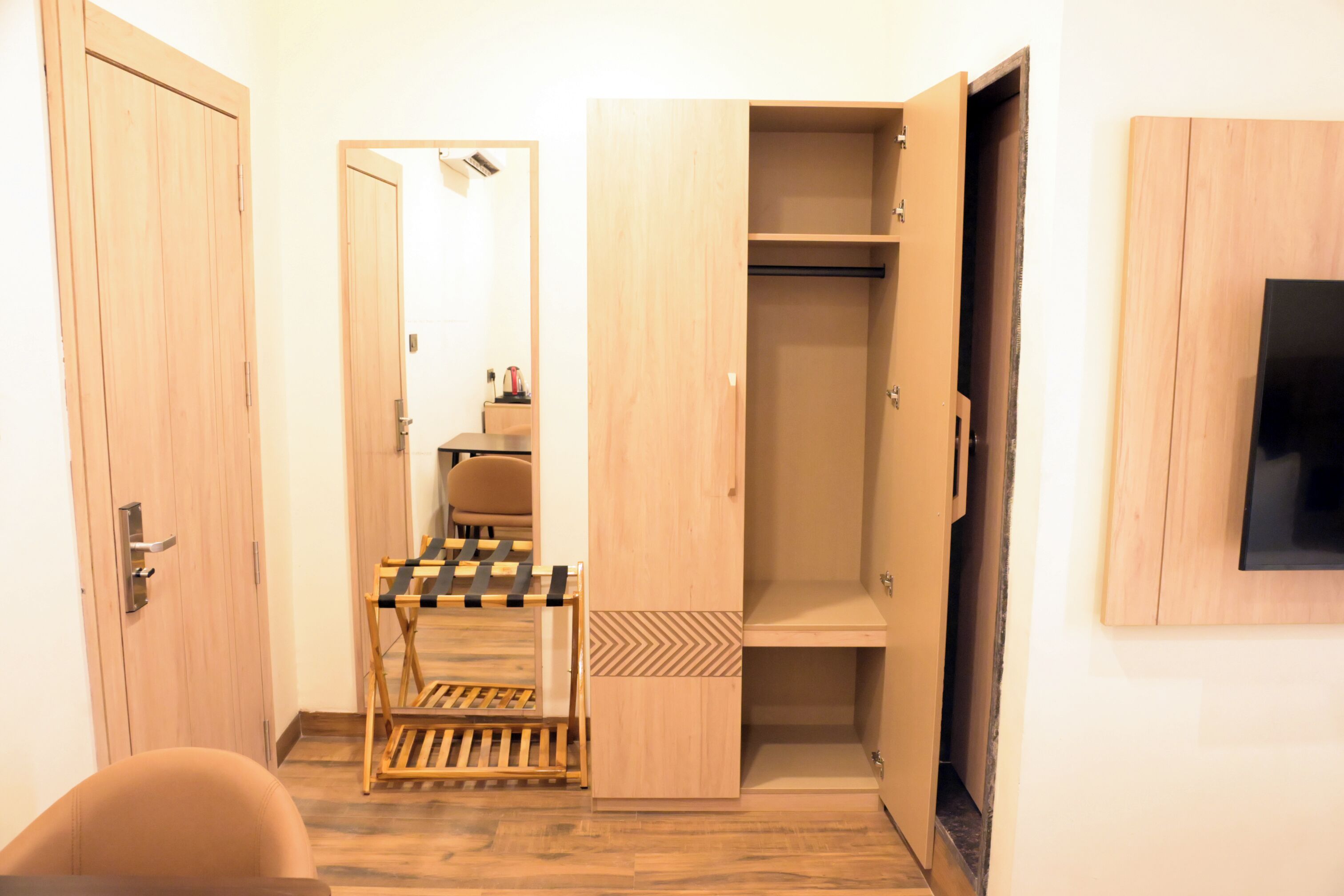 Une pièce comprenant une armoire en bois, une chaise, une petite table et un téléviseur fixé au mur.