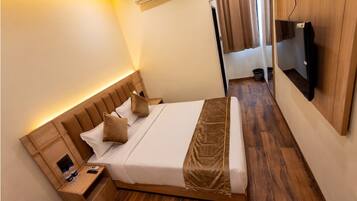 A neatly made bed with a headboard, a bedside table with a bottle and a phone, and a television mounted on the wall.