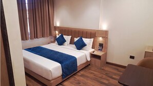 Ein Hotelzimmer mit einem großen Bett, einem hölzernen Kopfteil, zwei Kissen, einem Nachttisch mit Telefon und Wasserflaschen sowie einem kleinen Schreibtisch mit Stuhl.