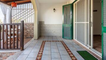 Un'area patio coperta con pavimento piastrellato, recinzione in legno e una porta con persiane verdi.