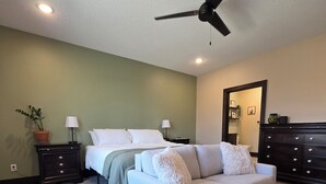 Une chambre à coucher avec un lit, un canapé blanc, une commode, un ventilateur de plafond et une plante en pot.