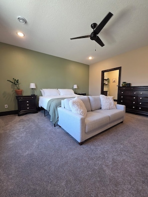 Une chambre à coucher avec un lit, un canapé blanc, une commode, un ventilateur de plafond et une plante en pot.