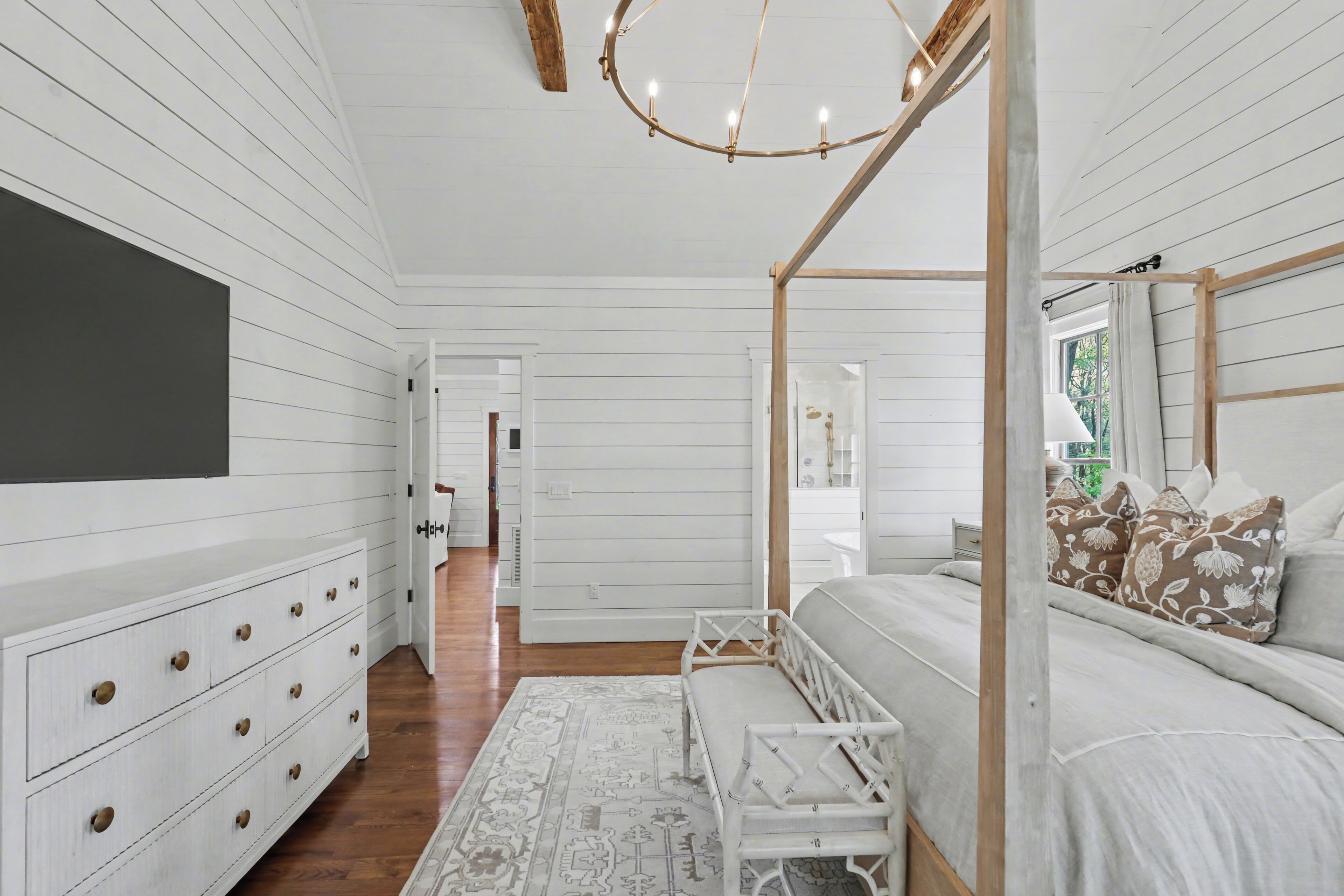 Un dormitorio con una cama con dosel, un aparador, un televisor y un pasillo que conduce a otra habitación.