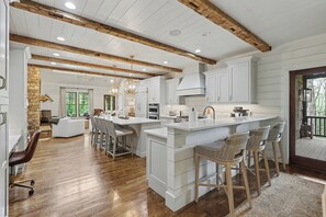 A spacious kitchen with wooden beams, white cabinetry, and a large island with bar stools.
