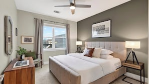 Ein Schlafzimmer mit einem Bett, Nachttischen, einem Deckenventilator, einem Fenster mit Vorhängen und Blick auf die Stadt.