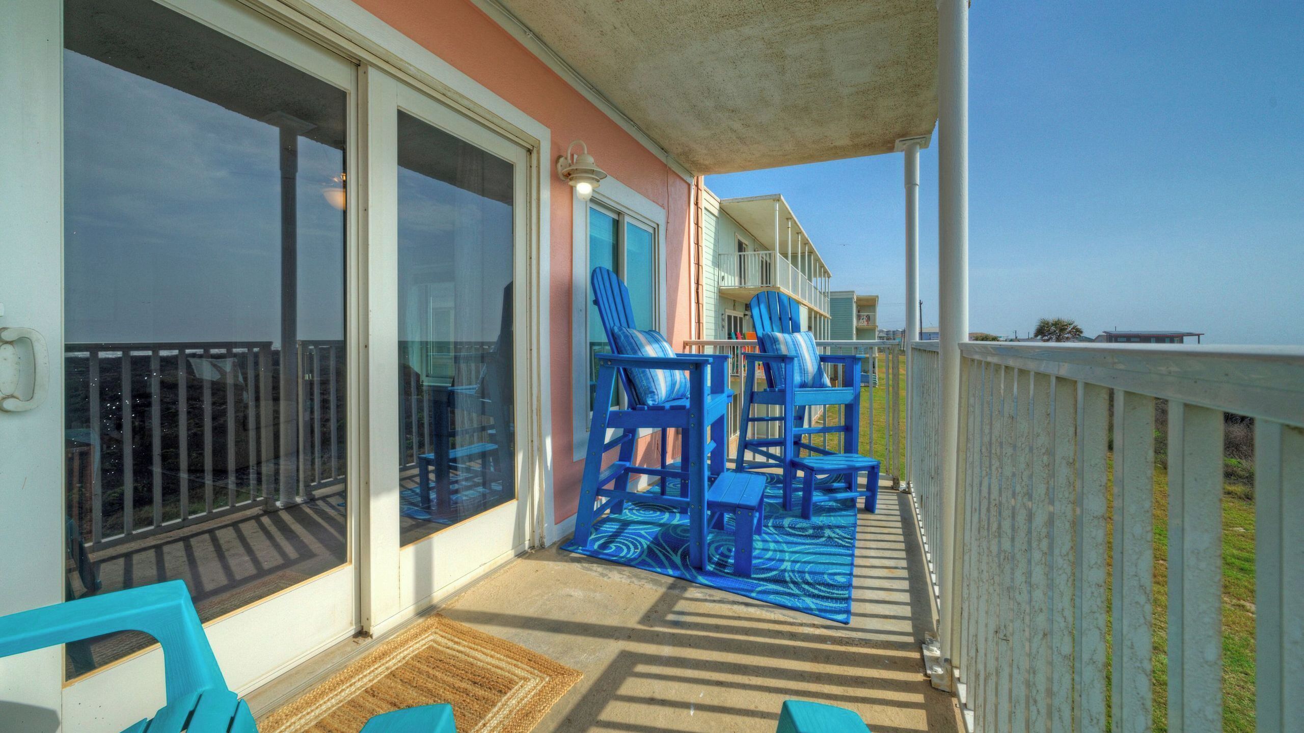 Un balcon avec des chaises bleues, une terrasse en bois et une vue sur l’océan.