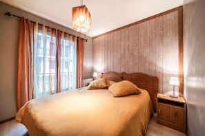 A bedroom with a wooden headboard, a bed with beige bedding, a nightstand with a lamp, and a window with curtains. - Ground floor, terrace, parking, tv, ski locker, 50m², Morzine (Morzine)