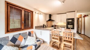 Eine kompakte Küche mit Essbereich, ein Sofa mit gemusterten Kissen und ein Fenster mit Jalousien.