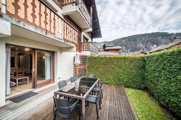 A modern outdoor dining area with a glass table and chairs, a wooden deck, and a view of a mountainous landscape. - Ground floor, terrace, parking, tv, ski locker, 50m², Morzine (Morzine)
