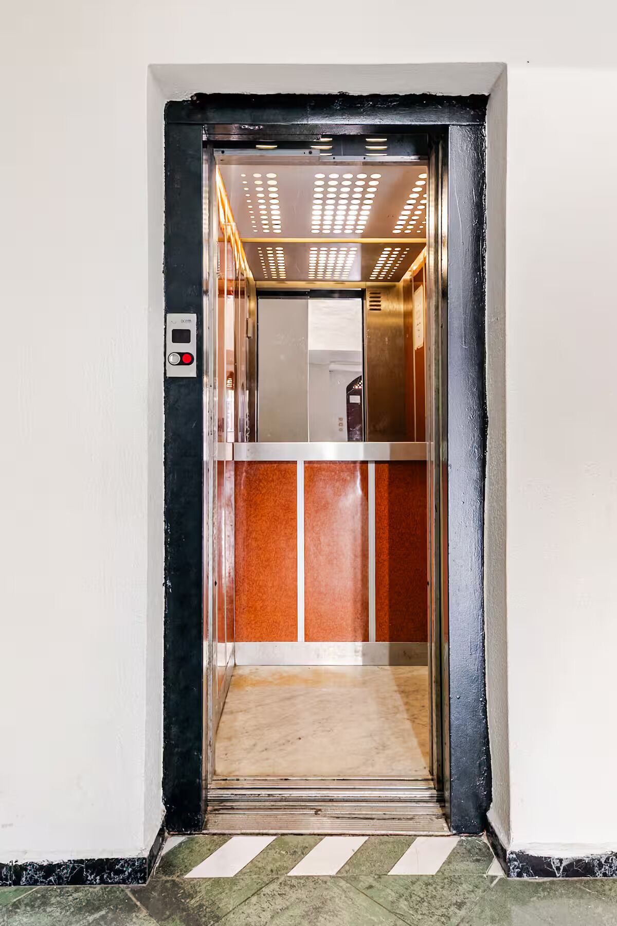 Un ascensor con panel de control, interior metálico y suelo de baldosas.