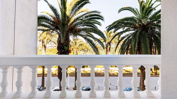 A balcony with white balustrades overlooking palm trees and a road with cars. - Lovely 2-El Jadida City Center Apt – Ideal Spot, Beach View & WiFi (El Jadida)