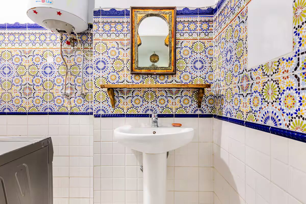 Une salle de bain avec un lavabo blanc, un miroir et un mur décoré de carreaux.