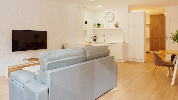 Uma sala moderna com sofá, televisão de tela plana, área de jantar com mesa e cadeiras, e cozinha com pia e bancada.