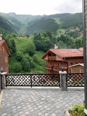 A building with a red-tiled roof, a balcony with a patterned railing, and a view of green hills in the background. - Goblec Hotel (Çaykara)