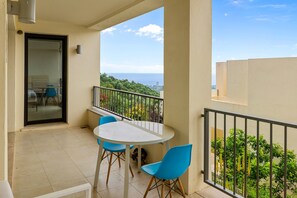 Ein Balkon mit Tisch und Stühlen, Blick auf das Meer und eine Tür zu einem Innenraum.
