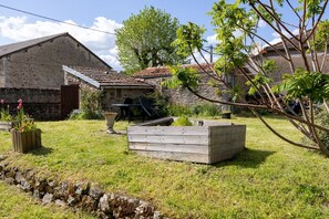 A rustic stone building with a tiled roof, a wooden bench, and a raised garden bed.