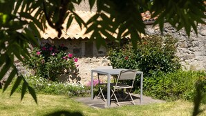 A garden with a table and chair, a stone wall, and flowering plants. - Gîte La Traverse: Private Terrace, Private Garden, and Wi-Fi in Persac (Persac)