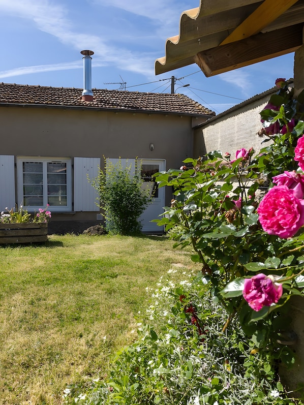 A house with a tiled roof, a chimney, a garden with flowers, and a wooden pergola.