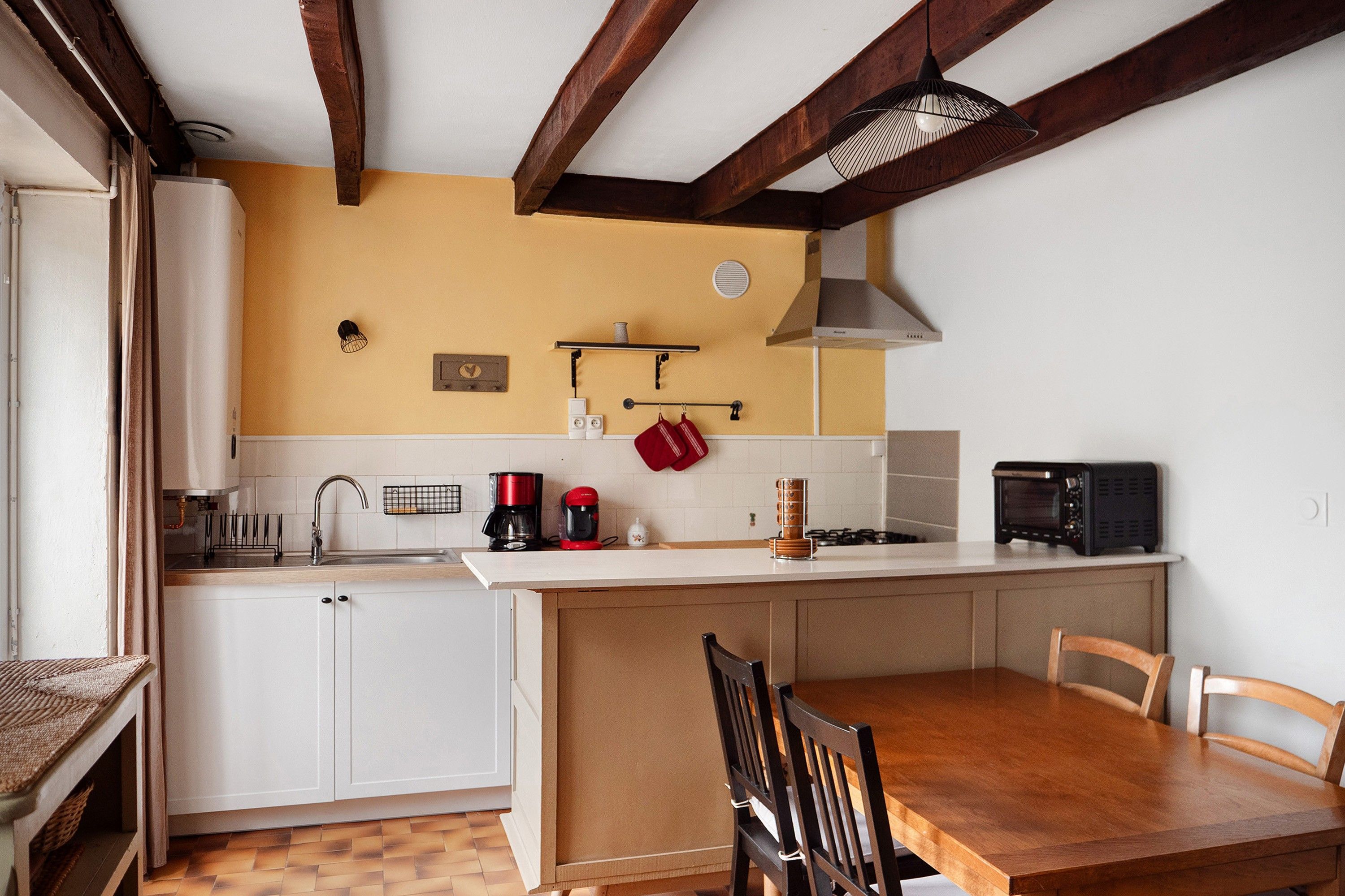 Een compacte keuken met witte kastjes, een houten eettafel en een ingebouwde magnetron.