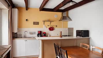 Een compacte keuken met witte kastjes, een houten eettafel en een ingebouwde magnetron.
