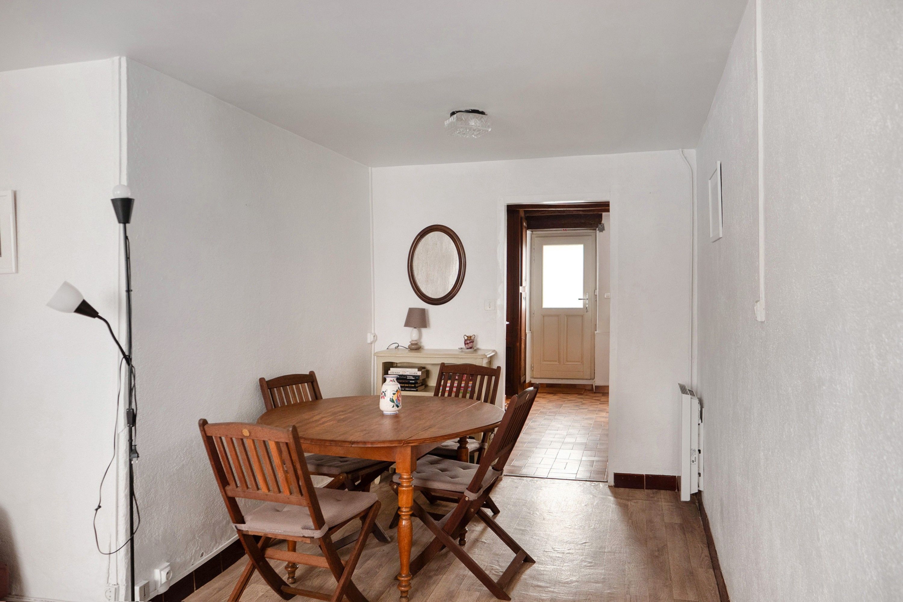 A dining room with a wooden table and chairs, a lamp, and a mirror on the wall.