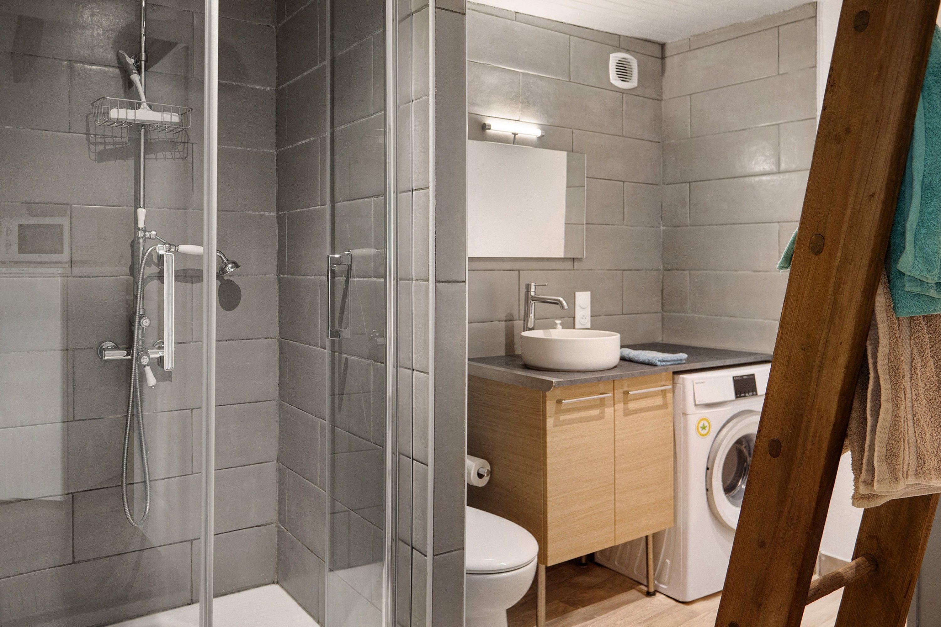 Ein modernes Badezimmer mit einer gläsernen Dusche, einem Waschbecken, einer Toilette und einer Waschmaschine.