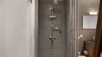 A modern bathroom with a glass-enclosed shower, a toilet, and a sink with a mirror above.