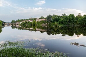 Ein ruhiger Fluss mit einer Brücke, Gebäuden und üppigem Grün.