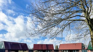 Un bâtiment avec un toit rouge, une porte verte et une haie devant.
