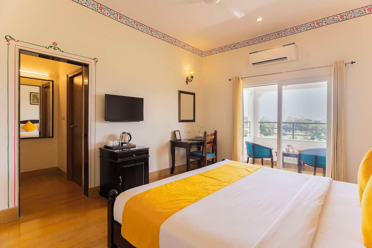 Una habitación de hotel con cama, escritorio, silla, televisor y balcón con vistas.