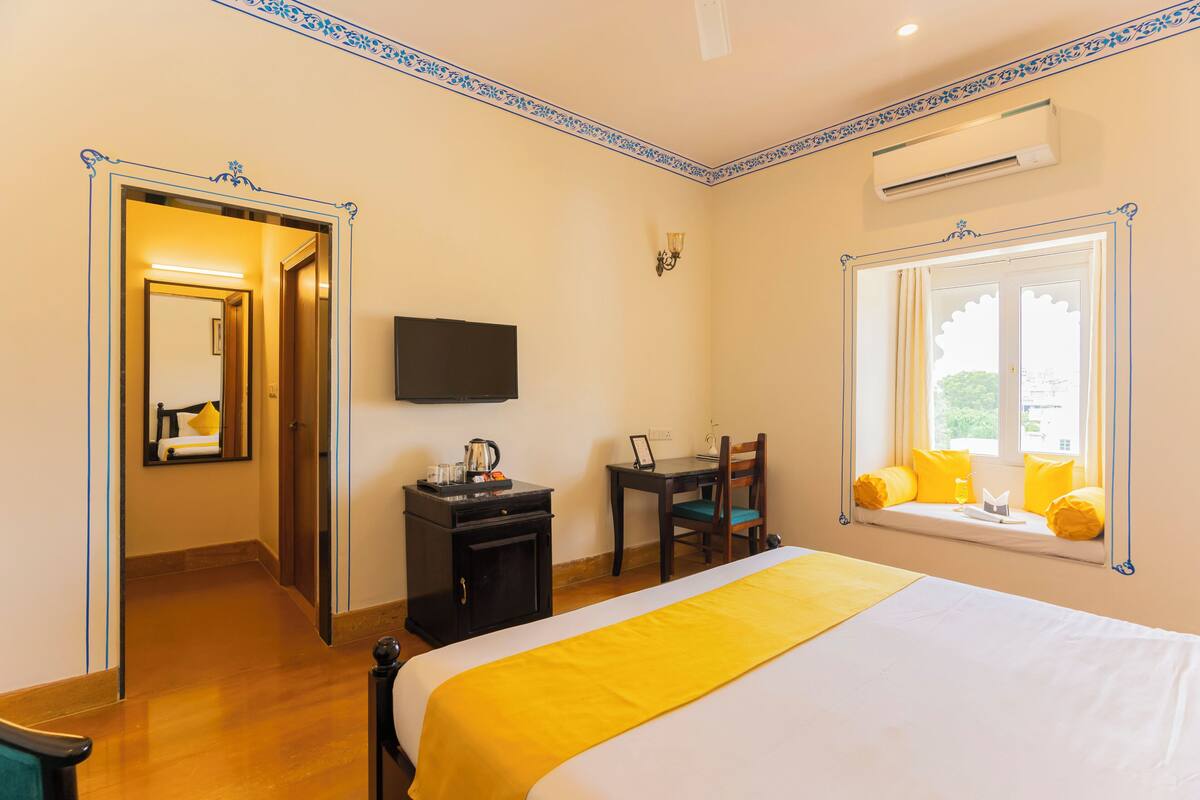 Habitación de hotel con cama, escritorio, silla, televisor y ventana con vista.