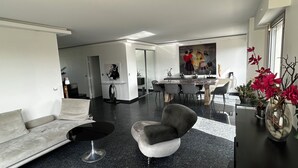 Un saló modern amb un sofà, una taula de centre rodona, una zona de menjador amb taula i cadires, i un quadre a la paret.