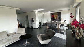 A modern living room with a sofa, a round coffee table, a dining area with a table and chairs, and a painting on the wall. - Terrace apartment in Père Lachaise, exceptional light and view (Paris)