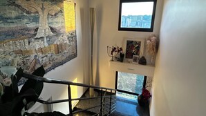 Una escala amb barana metàl·lica, una vista de la ciutat a través d'una finestra i una obra d'art mosaic a la paret.