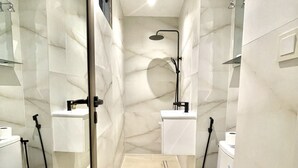 Un baño moderno con separador de vidrio, dos inodoros, ducha y lavamanos.