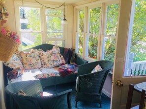 Une pièce chaleureuse avec un canapé en osier, un fauteuil et une table agrémentée d’un coussin à motifs floraux.