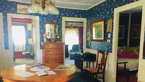 A room with a wooden dining table, a dresser, a mirror, a blue patterned wall, and a doorway leading to another room.