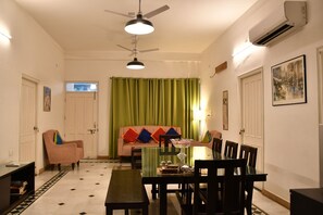 A dining area with a table, chairs, a bench, a ceiling fan, and an air conditioning unit. - Nawab Ki Deohri - A Boutique Heritage Homestay (Varanasi)