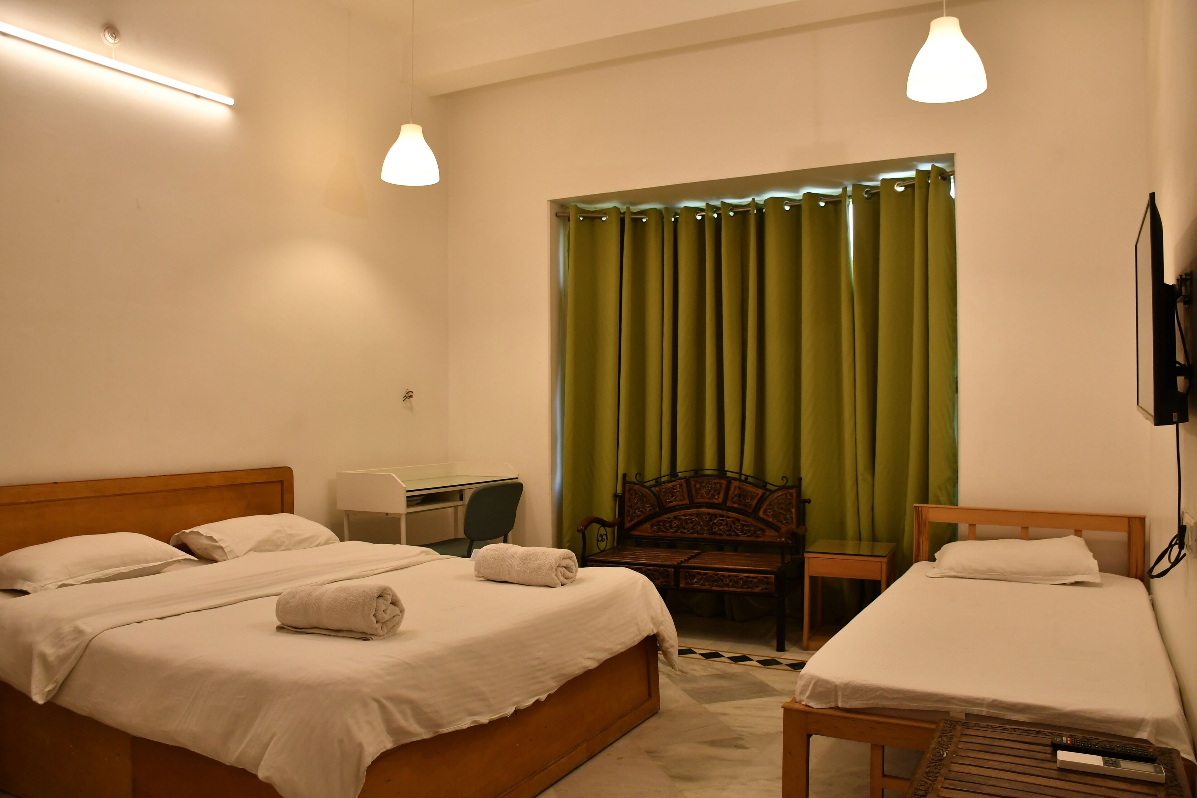 A hotel room with two beds, a desk, a chair, a television, and a window with curtains.