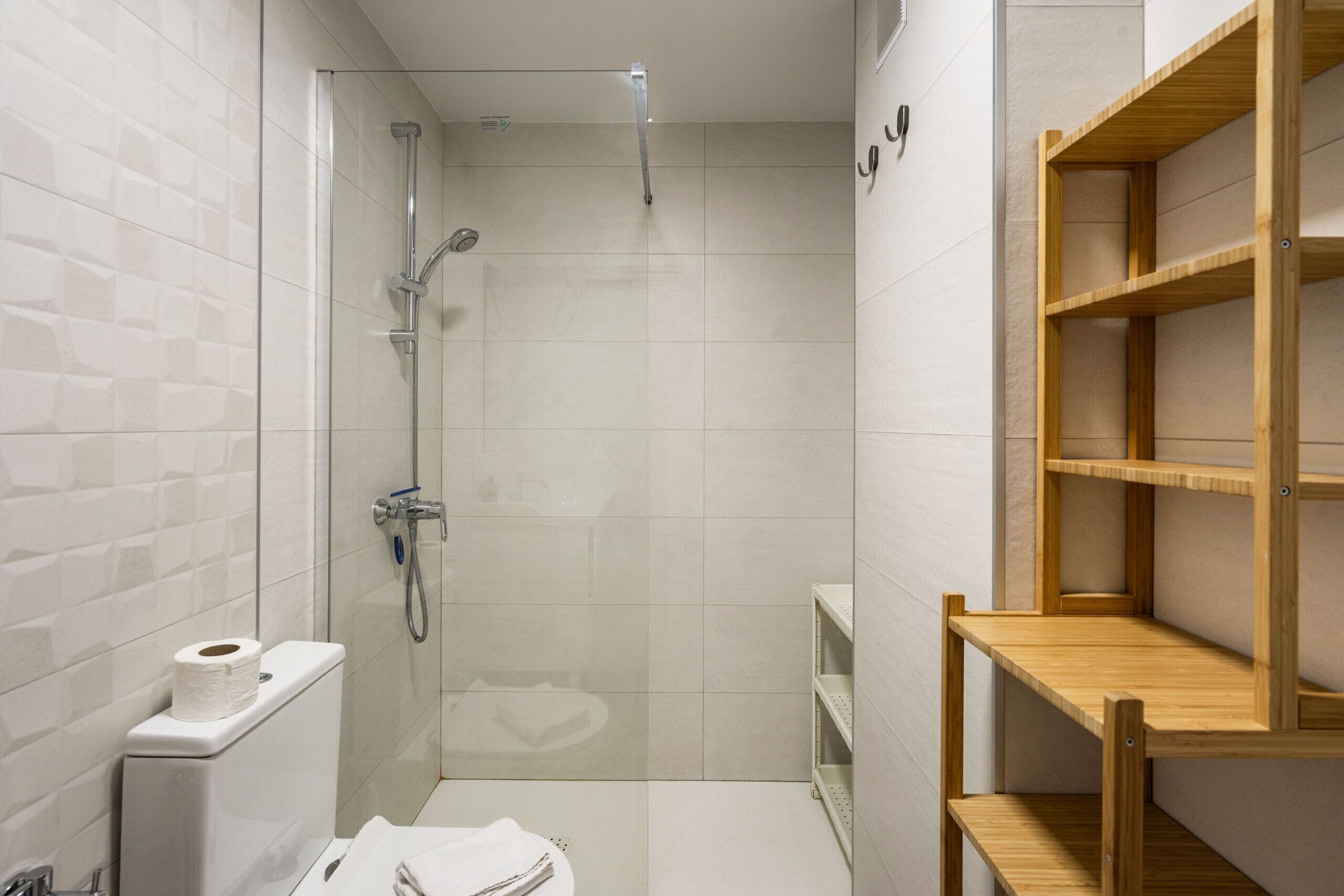 Un baño con ducha, inodoro y estantería de madera.