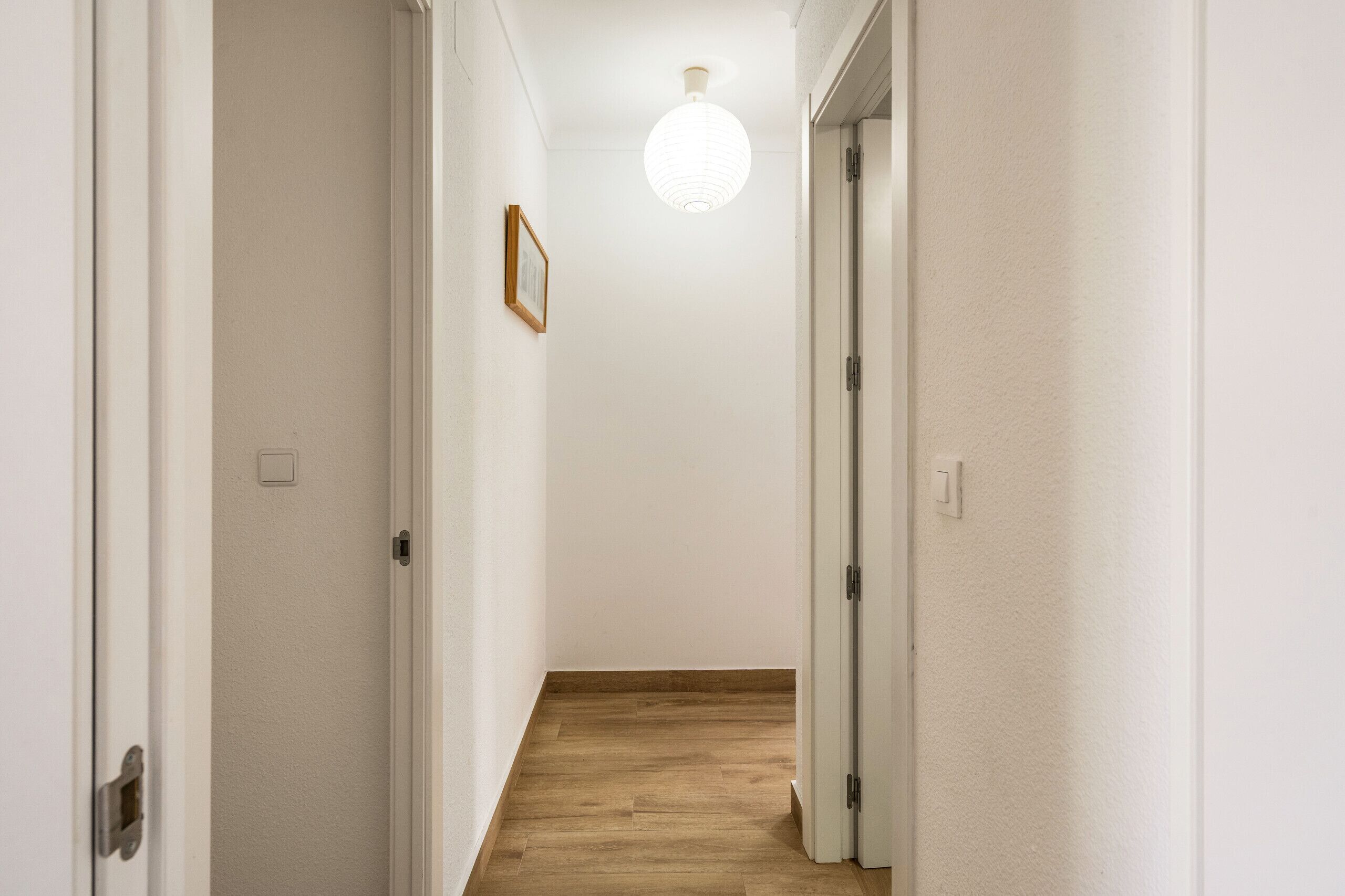 A narrow hallway with wooden flooring, white walls, and a single light fixture.