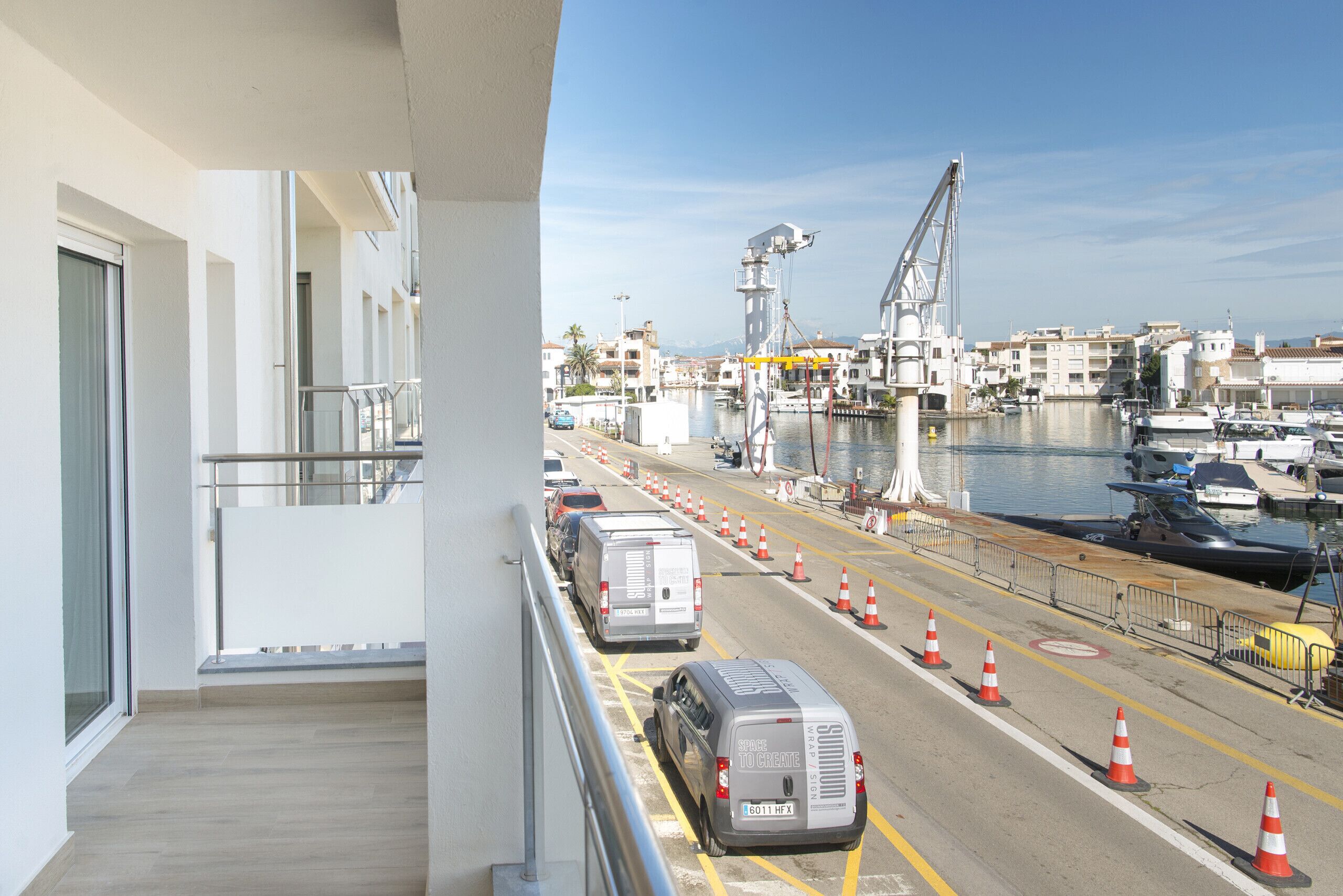 A balcony with a view of a marina, parked vehicles, and a clear sky.